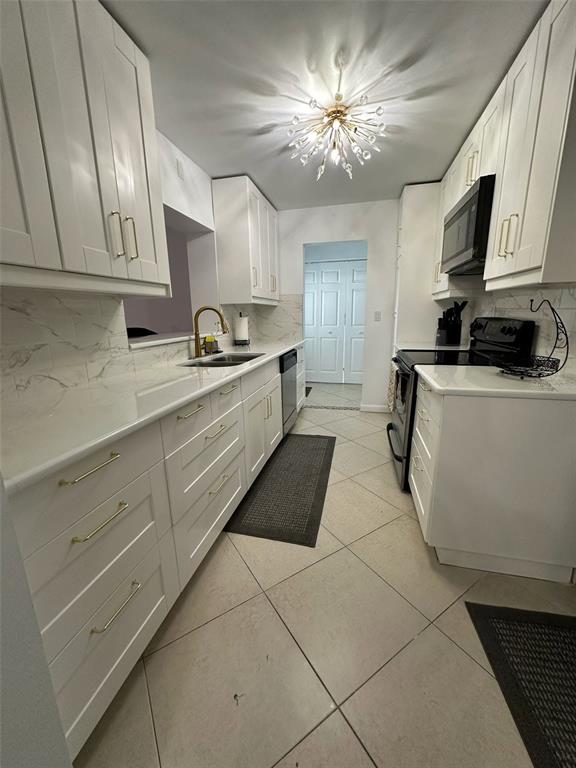 A galley kitchen features white cabinets, marble-look countertops, stainless steel appliances, and a modern chandelier — 1211 LEHIGH STREET, KISSIMMEE, FL