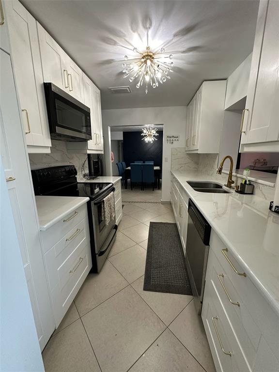 A galley kitchen features white cabinets, quartz countertops, stainless steel appliances, and a modern chandelier — 1211 LEHIGH STREET, KISSIMMEE, FL