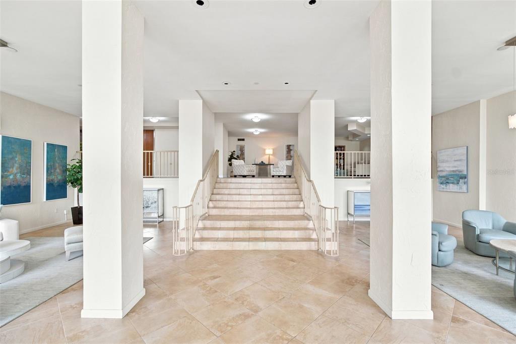 A spacious lobby features a central tiled staircase flanked by white columns and seating areas — 707 S GULFSTREAM AVENUE UNIT 207, SARASOTA, FL