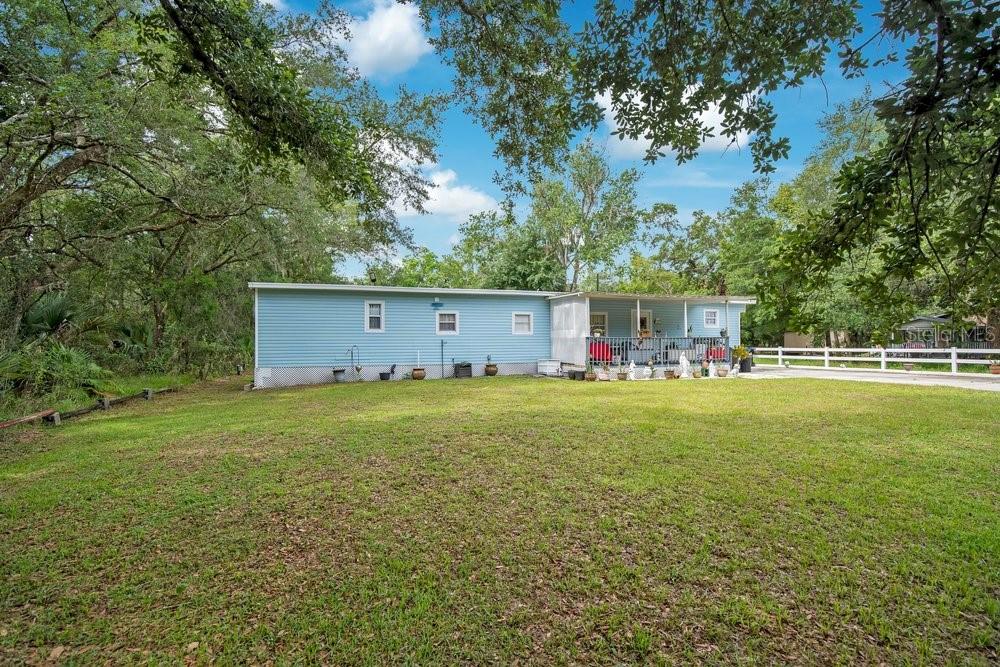 A light blue manufactured home sits on a grassy lot surrounded by mature trees — 18222 LYNBROOK ROAD, ORLANDO, FL