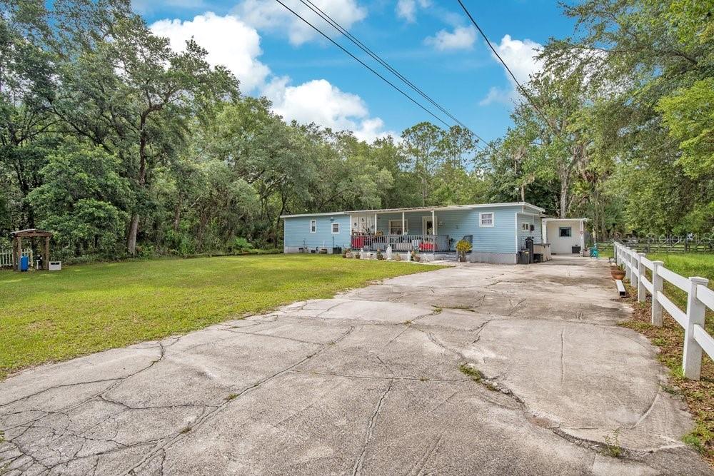 A light blue single-story house with a front porch sits behind a large cracked driveway — 18222 LYNBROOK ROAD, ORLANDO, FL
