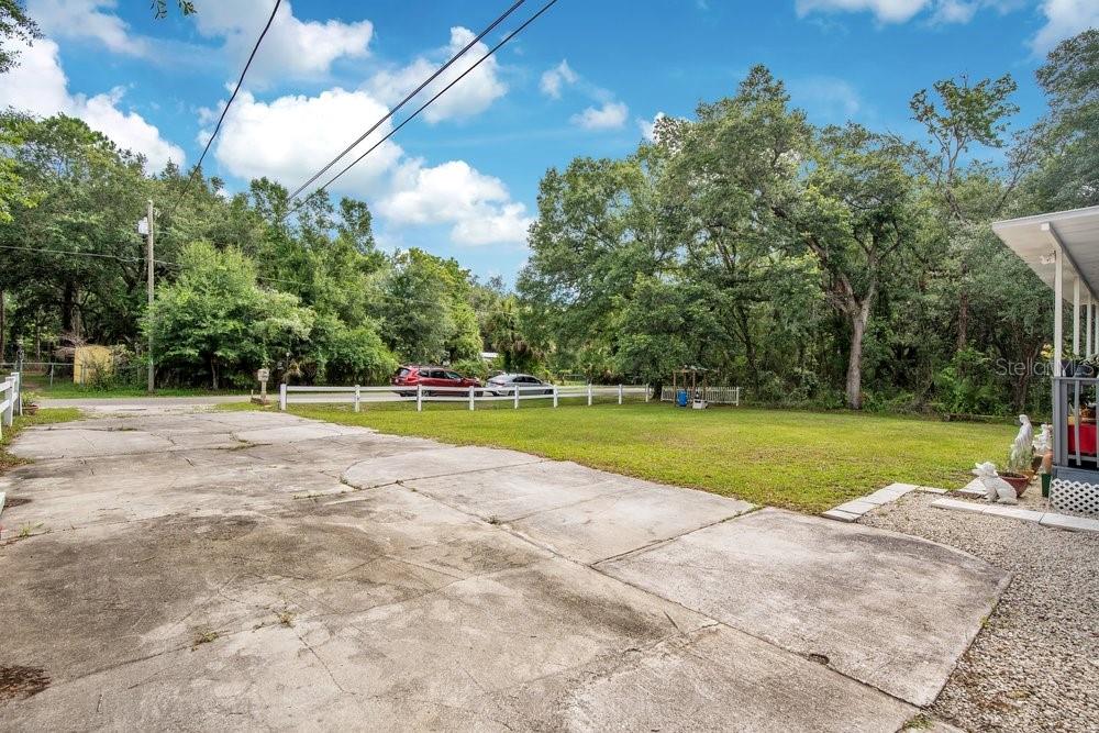 A concrete driveway leads to a grassy yard bordered by a white fence and trees — 18222 LYNBROOK ROAD, ORLANDO, FL