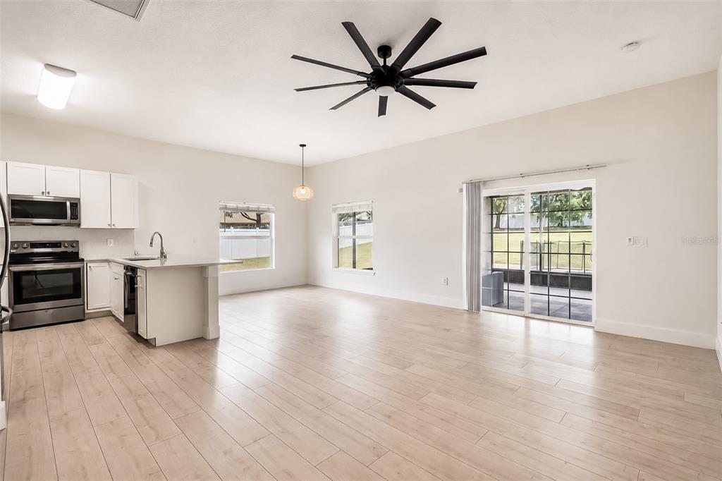 An open-concept kitchen and living area features white cabinetry, stainless appliances, and light wood flooring — 10105 LENOX STREET, CLERMONT, FL
