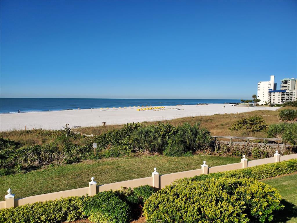 An elevated view of a sandy beach, dunes, and a distant hotel under a clear sky — 6650 SUNSET WAY UNIT 220, ST PETE BEACH, FL