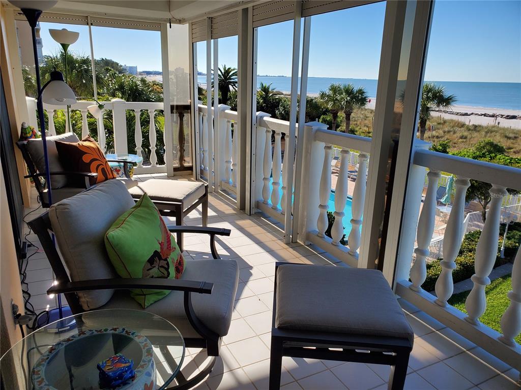 A screened balcony features tiled flooring, patio furniture, and a view of the ocean — 6650 SUNSET WAY UNIT 220, ST PETE BEACH, FL