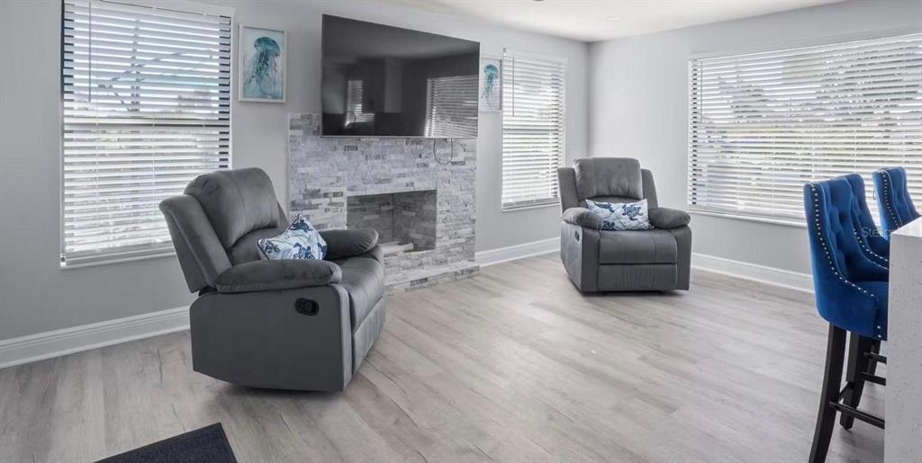 A living room features two gray recliners, a stone fireplace with a television, and light flooring — 6712 SEA RANCH DRIVE, HUDSON, FL
