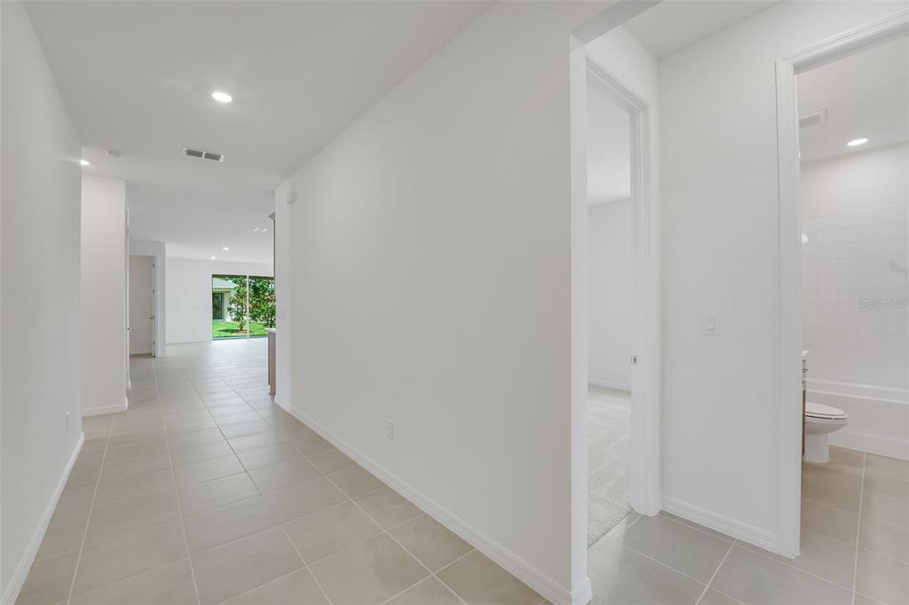 A hallway with light tile flooring leads to a living area with sliding glass doors — 13512 TURNLEAF BOULEVARD, PUNTA GORDA, FL
