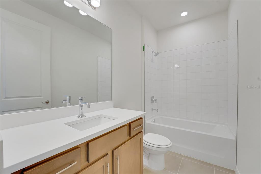 A bathroom features a light wood vanity, white countertop, large mirror, and a tiled tub-shower — 13512 TURNLEAF BOULEVARD, PUNTA GORDA, FL