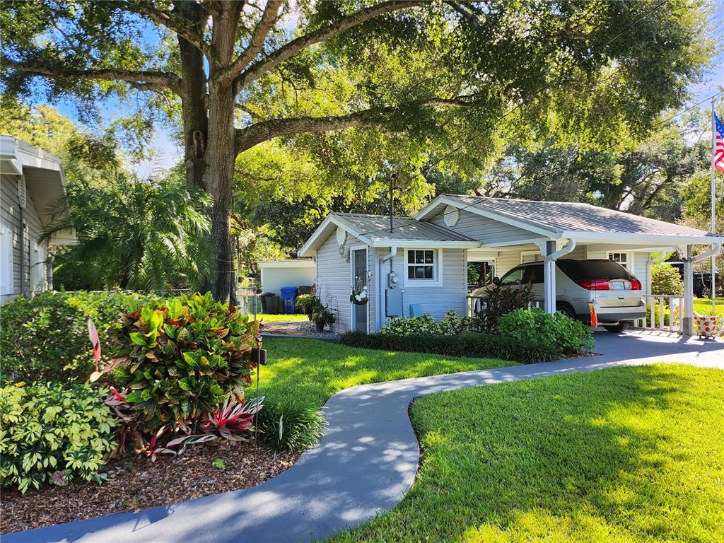 A gray house with a carport and a curved walkway sits under large shade trees — 411 BRYAN ROAD, BRANDON, FL