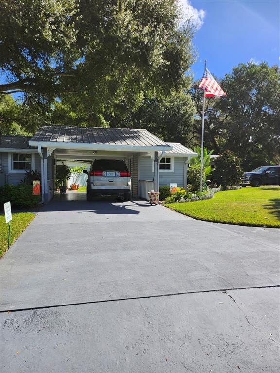 A gray house with a metal-roofed carport and a driveway featuring an American flag — 411 BRYAN ROAD, BRANDON, FL