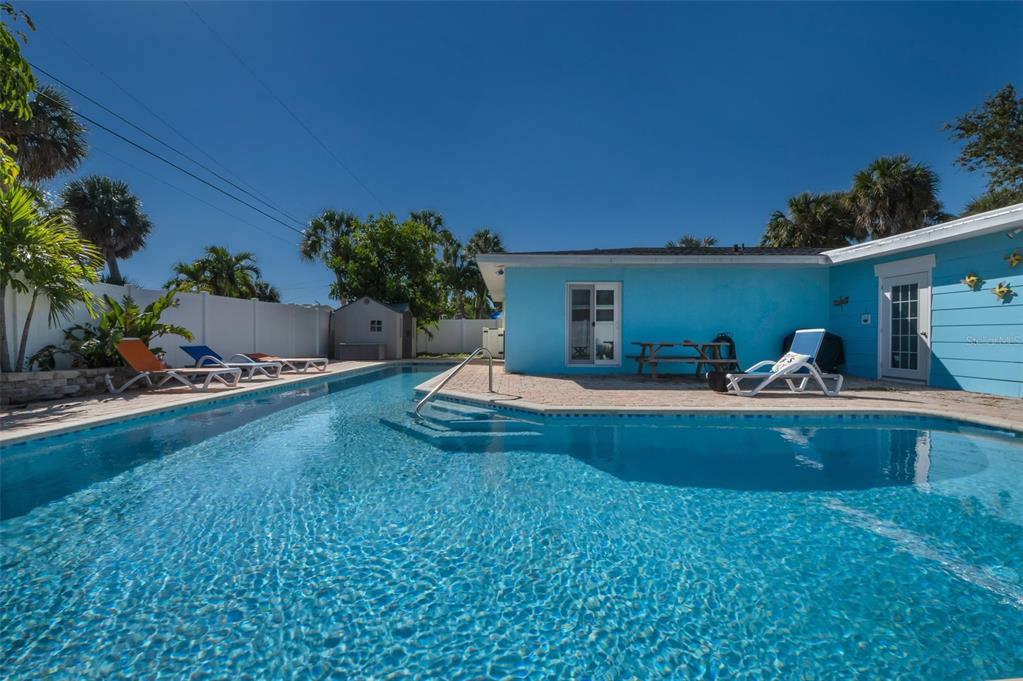 A bright blue house with a swimming pool, patio furniture, and a white privacy fence — 424 88TH AVENUE, ST PETE BEACH, FL