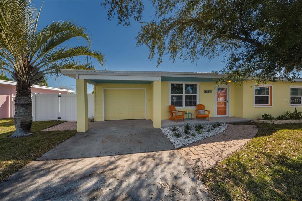 A yellow single-story house features a carport, a paved walkway, and two orange chairs — 424 88TH AVENUE, ST PETE BEACH, FL