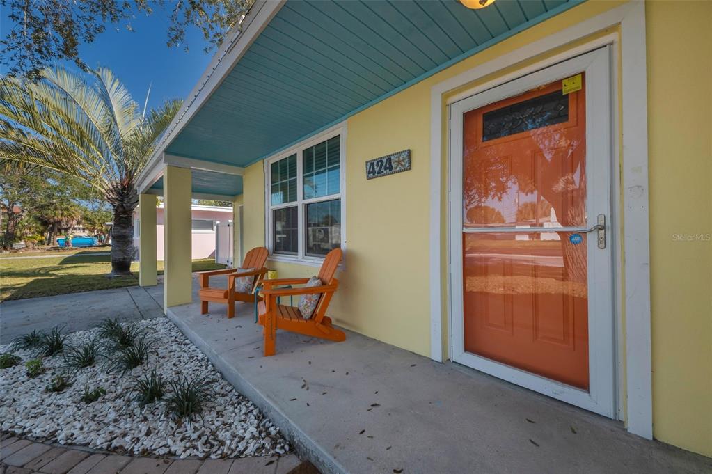A yellow house exterior features a covered porch with two orange chairs and a door — 424 88TH AVENUE, ST PETE BEACH, FL