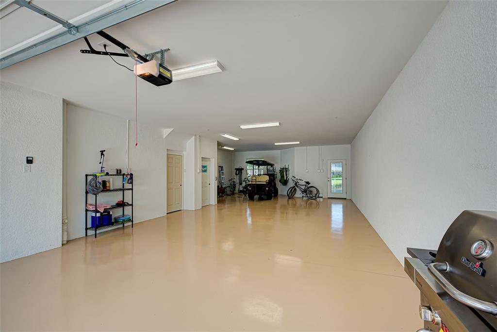 A spacious, well-lit garage with a light-colored epoxy floor, storage shelving, and a golf cart — 10345 LONGSHORE ROAD UNIT 29, PLACIDA, FL