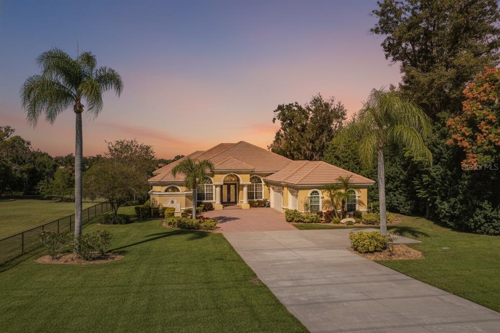 A single-story yellow stucco house with a tile roof and palm trees at sunset — 2918 CLUBHOUSE ROAD, LAKELAND, FL