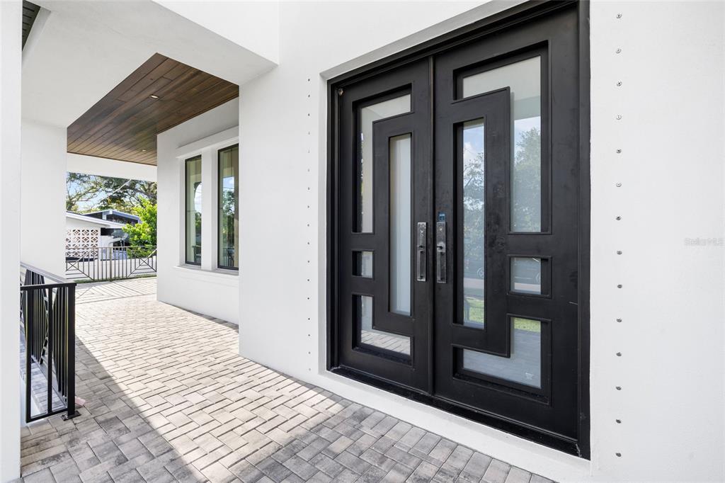 A modern double front door with geometric glass panels opens onto a paved entryway porch — 5025 W DANTE AVENUE, TAMPA, FL