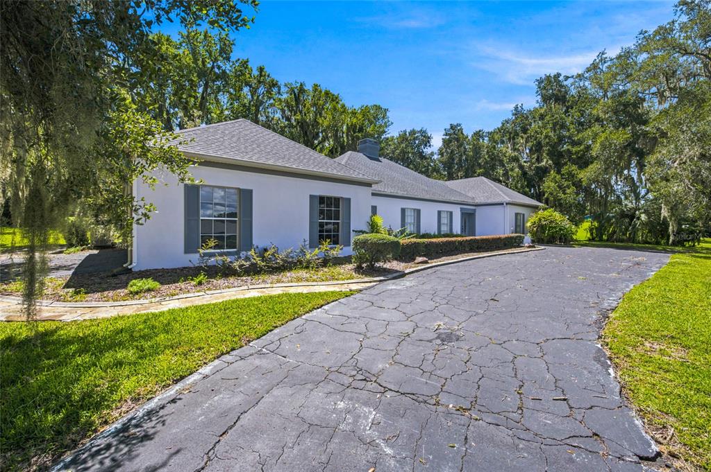 A white single-story house with a cracked asphalt driveway and surrounding trees — 7860 NW 56TH PLACE, OCALA, FL