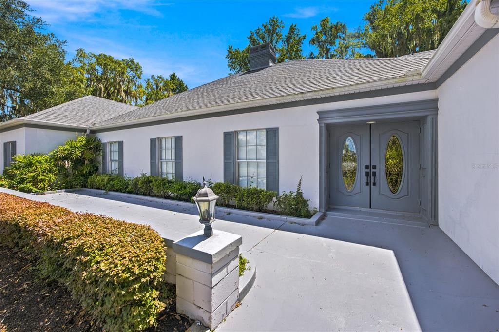 A white house exterior features a gray double front door, shutters, and a concrete walkway — 7860 NW 56TH PLACE, OCALA, FL