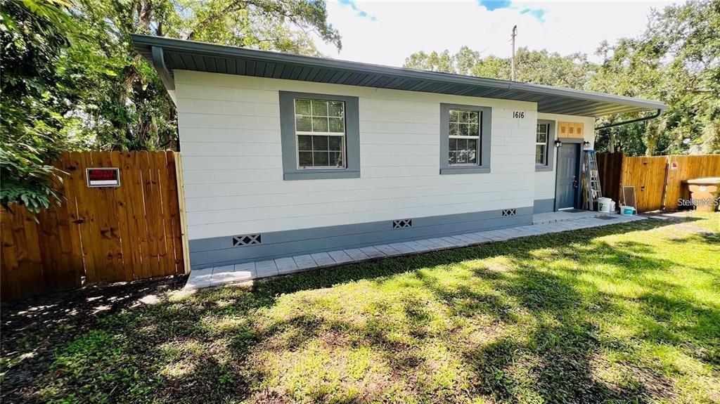 The exterior of a single-story house features white block walls, gray trim, and a wooden fence — 1616 HOPE STREET, INTERCESSION CITY, FL