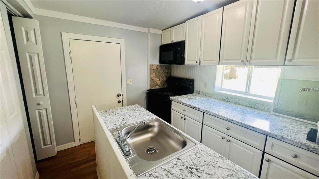 A kitchen features white cabinets, granite countertops, a stainless steel sink, and black appliances — 1616 HOPE STREET, INTERCESSION CITY, FL