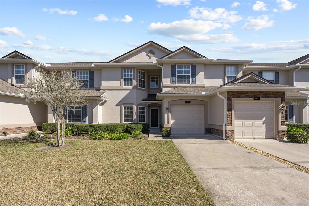 A two-story townhouse with a beige stucco exterior, two garages, and a front lawn — 466 WOODED CROSSING CIRCLE, ST AUGUSTINE, FL