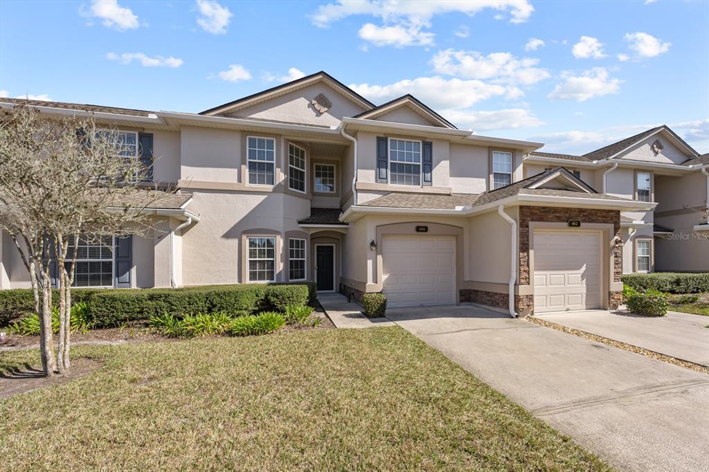 A two-story townhouse with a beige stucco exterior, two garages, and a front lawn — 466 WOODED CROSSING CIRCLE, ST AUGUSTINE, FL