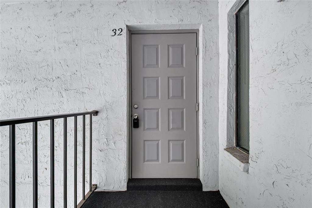 A gray front door with eight panels is set into a white textured exterior wall — 8201 SUN SPRING CIRCLE UNIT C2, ORLANDO, FL