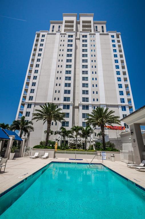 A tall, light-colored residential building stands behind a rectangular swimming pool on a sunny day — 331 CLEVELAND STREET UNIT 312, CLEARWATER, FL
