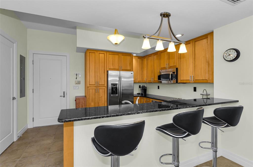 A kitchen features wooden cabinets, stainless steel appliances, a granite breakfast bar, and bar stools — 331 CLEVELAND STREET UNIT 312, CLEARWATER, FL