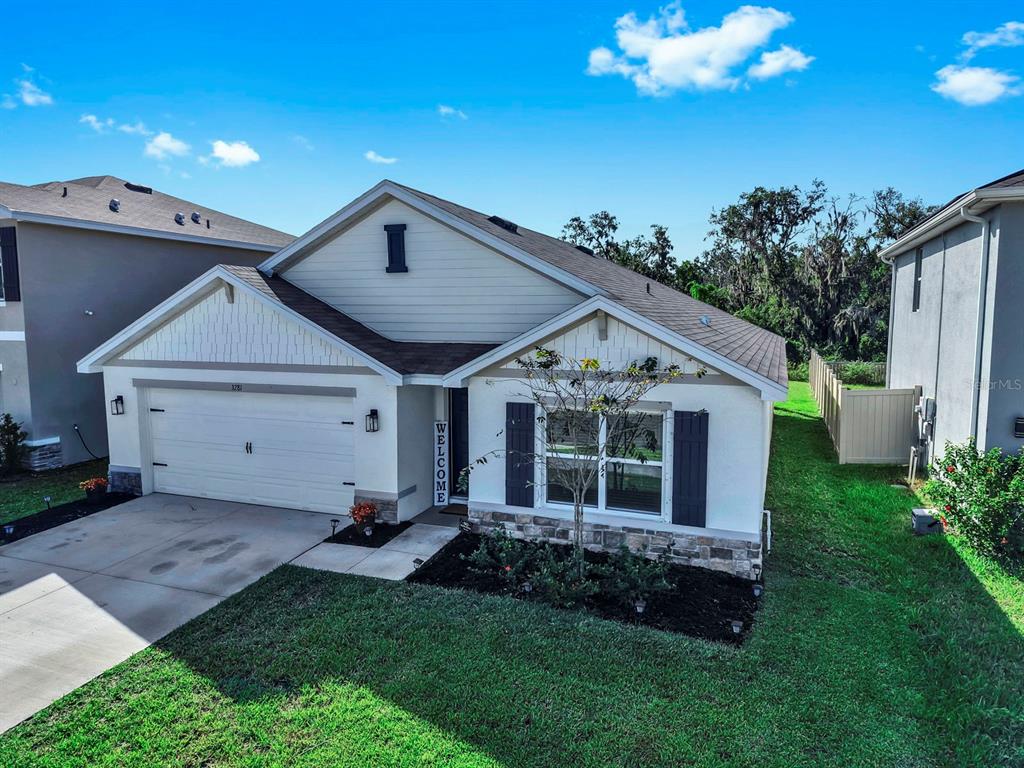 An exterior view of a single-story suburban house with a two-car garage and stone accents — 3281 SILVER DATE DRIVE, WIMAUMA, FL