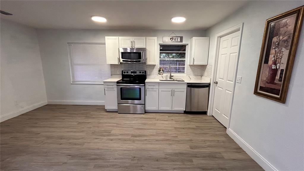 A kitchen features white cabinets, stainless steel appliances, and light wood-look flooring — 519 DENSON STREET, COCOA, FL