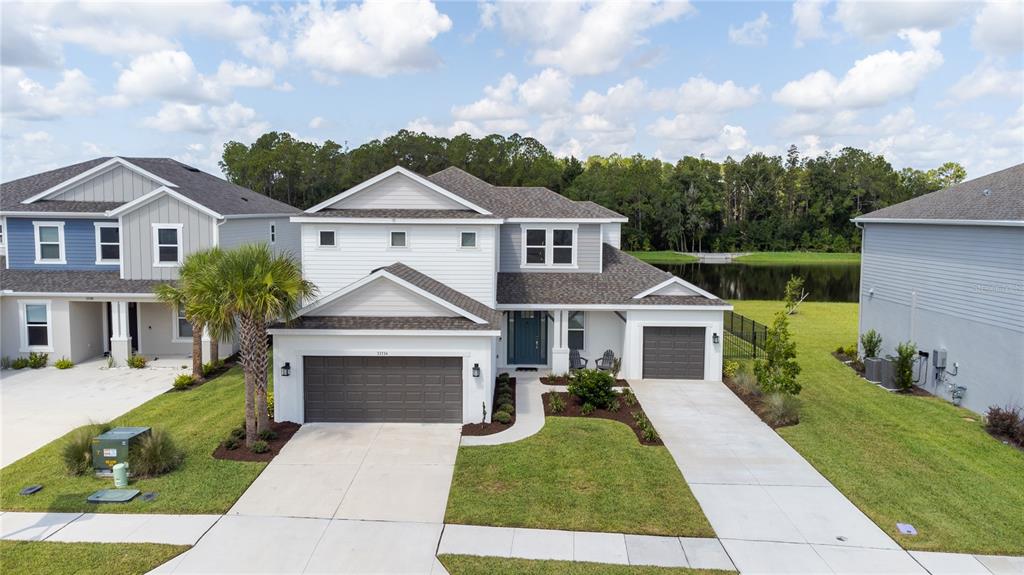 An aerial view shows a two-story suburban house with a three-car garage and a pond — 33734 LANDSMAN LOOP, WESLEY CHAPEL, FL