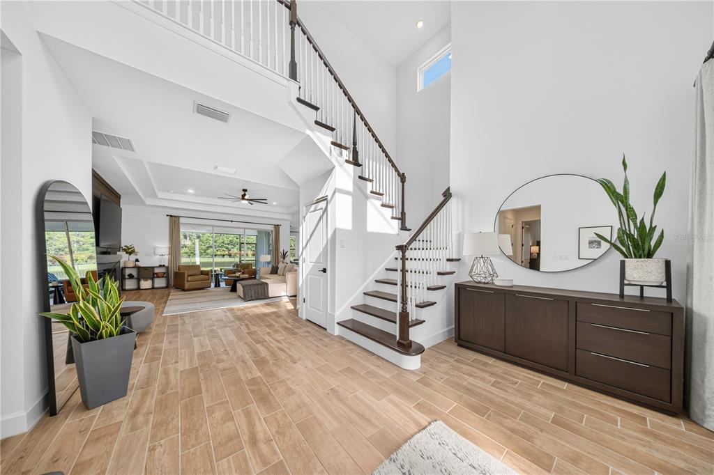A bright entryway features a wooden staircase, tile flooring, a console table, and a mirror — 33734 LANDSMAN LOOP, WESLEY CHAPEL, FL