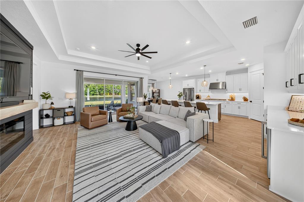 An open-concept living room and kitchen featuring a fireplace, sectional sofa, and wood-look tile flooring — 33734 LANDSMAN LOOP, WESLEY CHAPEL, FL