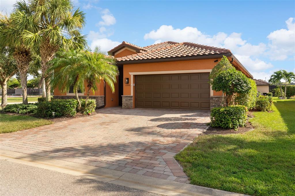 A single-story house with a terracotta tile roof, orange stucco walls, and a brick driveway — 11068 CHERRY LAUREL DR., FORT MYERS, FL