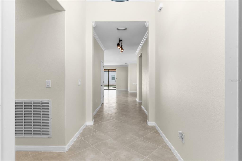 A bright hallway with light-colored walls and tiled flooring leads toward a glass-paned exterior door — 11068 CHERRY LAUREL DR., FORT MYERS, FL