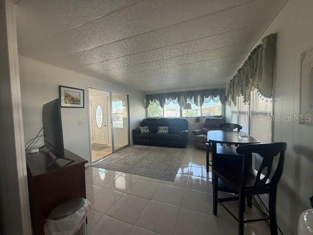 A living room with tile floors, a dark sofa, a dining set, and a television — 294 COLONIAL BOULEVARD UNIT 48, PALM HARBOR, FL