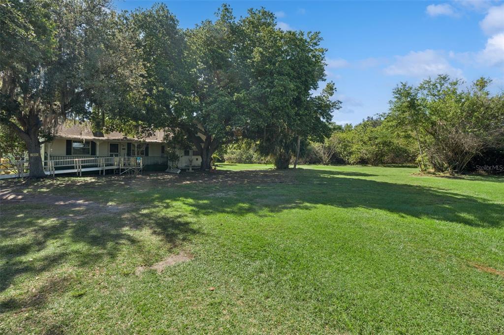 A single-story house with a wooden deck sits on a large, grassy lot with trees — 1235 HACKNEY ROAD, ST CLOUD, FL