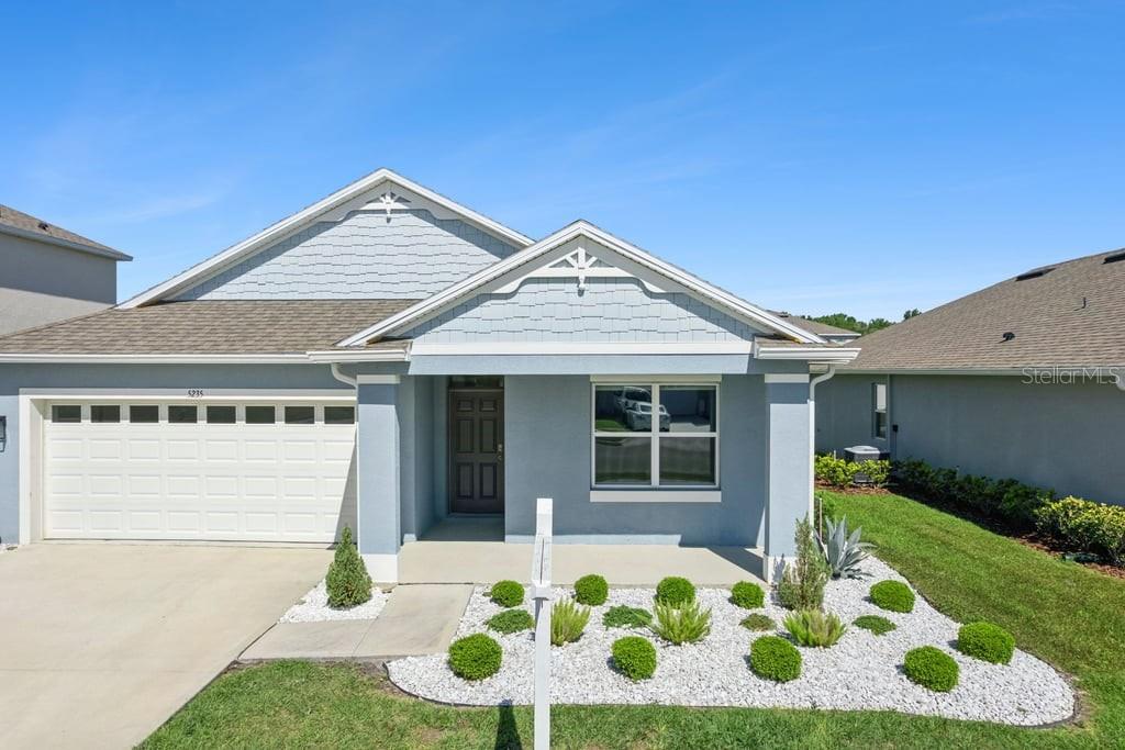 A light blue single-story house features a white garage door and a landscaped front yard — 5235 MAHOGANY DRIVE, MOUNT DORA, FL