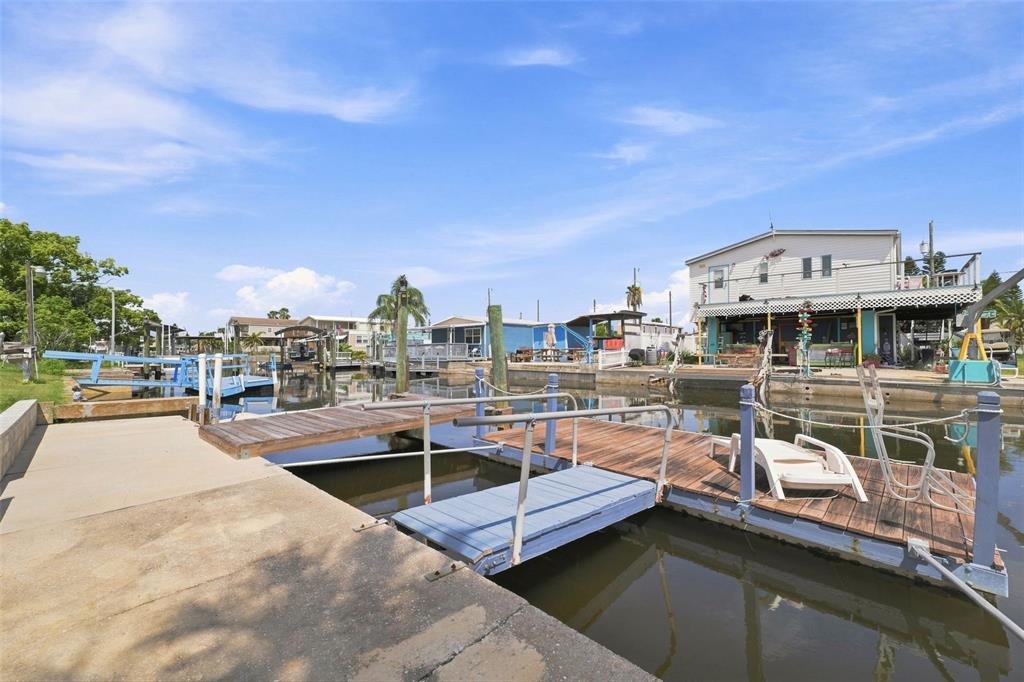 A concrete dock leads to a wooden floating pier on a canal with nearby houses — 6819 HERON LANE, HUDSON, FL