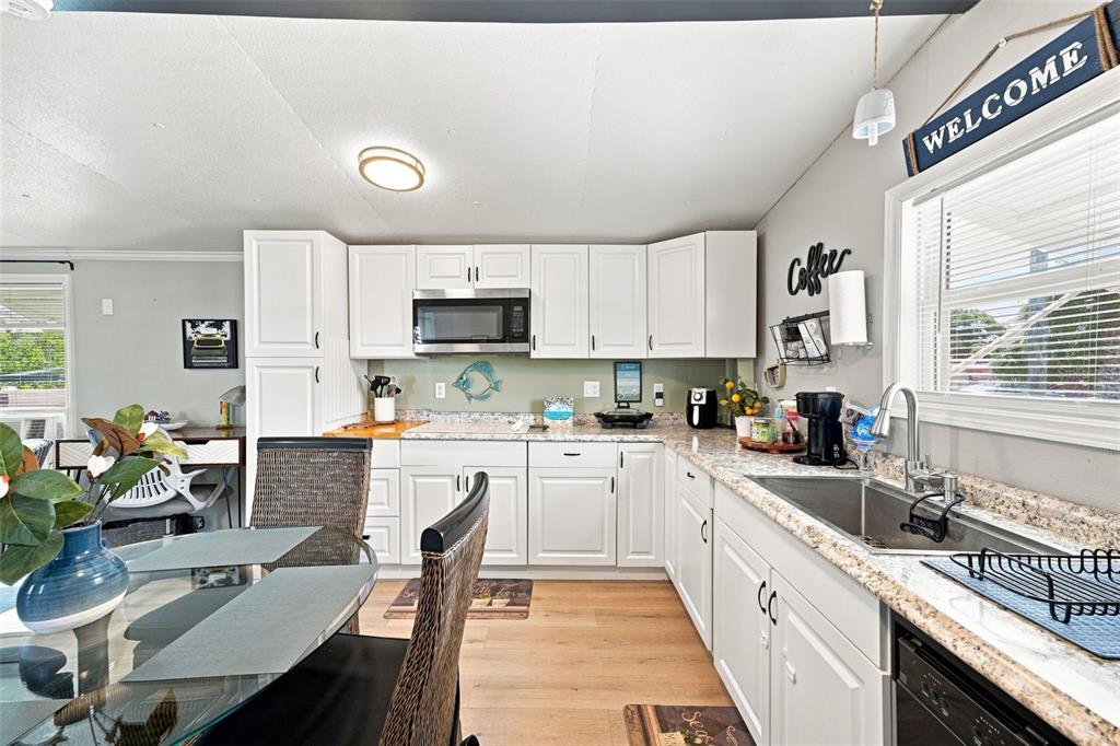 A kitchen features white cabinets, granite countertops, stainless steel appliances, and a glass dining table — 6819 HERON LANE, HUDSON, FL