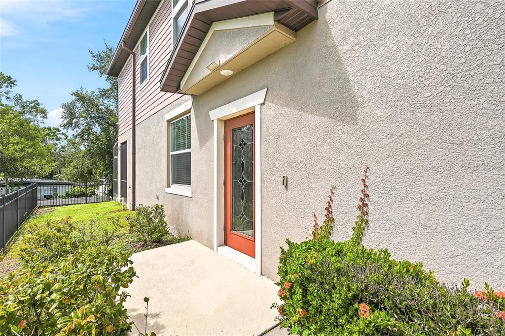 A side view of a house exterior featuring a red door, stucco walls, and landscaping — 5304 SYLVESTER LOOP, TAMPA, FL