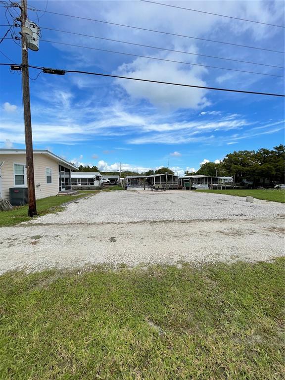 A gravel lot sits between a light-colored house and several mobile homes under a blue sky — 21728 73 LANE, VERO BEACH, FL