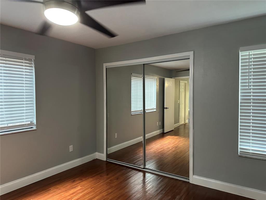 A bedroom with gray walls, wood-look flooring, two windows with blinds, and mirrored closet doors — 823 SW 58TH TERRACE, GAINESVILLE, FL