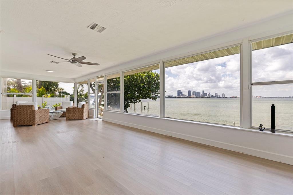 A sunroom with light wood floors features large windows overlooking a bay and city skyline — 501 22ND AVENUE SE, ST PETERSBURG, FL