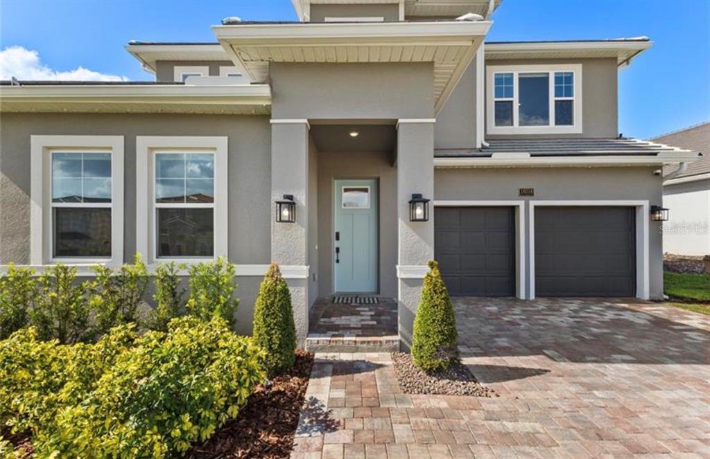 The exterior of a two-story house features a light blue front door and a two-car garage — 16018 VOLTERRA POINT, BELLA COLLINA, FL