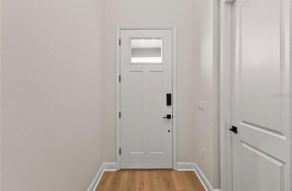 A white front door with a small window and black hardware in a neutral entryway — 16018 VOLTERRA POINT, BELLA COLLINA, FL