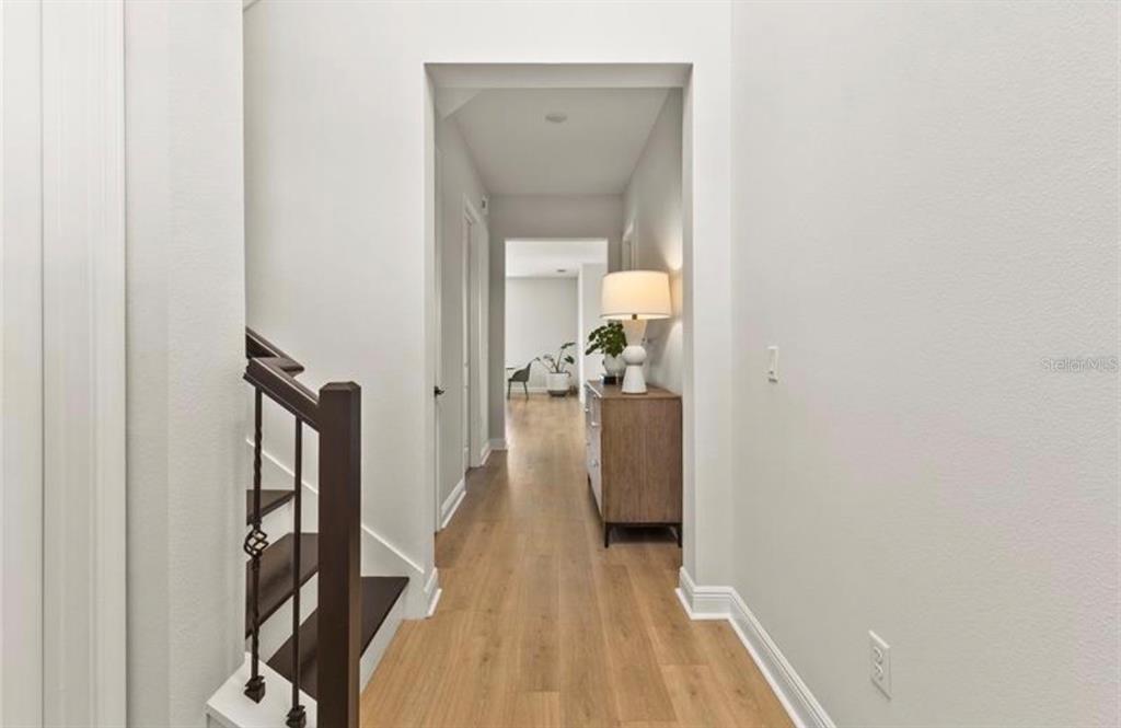 A hallway with light wood flooring leads past a staircase to an open living area — 16018 VOLTERRA POINT, BELLA COLLINA, FL