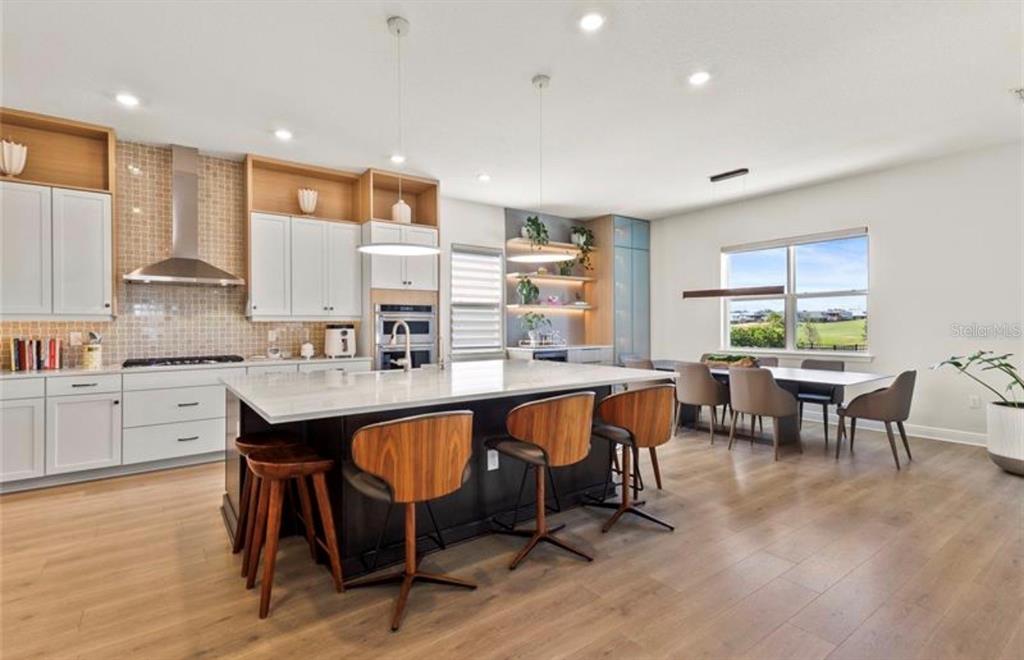 A modern kitchen features a large island with bar stools, white cabinetry, and wood flooring — 16018 VOLTERRA POINT, BELLA COLLINA, FL