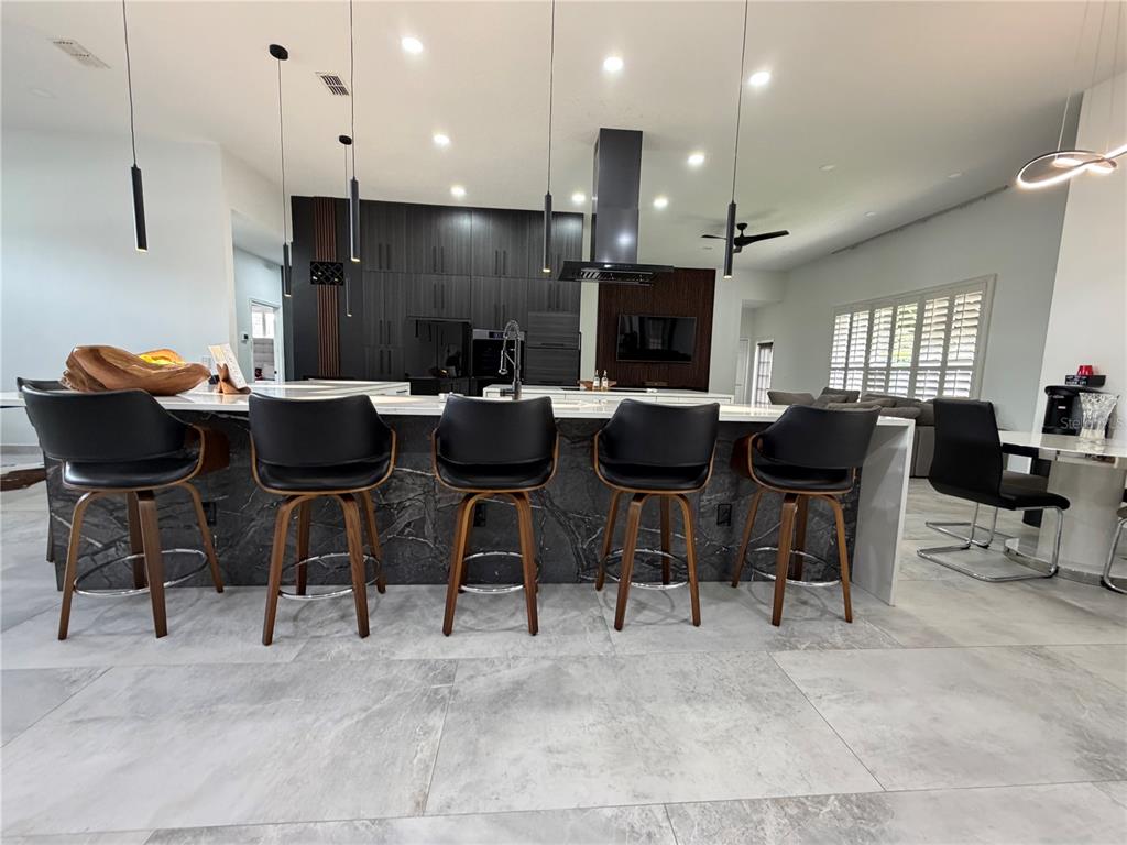 A modern kitchen features a large marble-topped island with five black stools and dark cabinetry — 4419 SADDLEWORTH CIRCLE, ORLANDO, FL